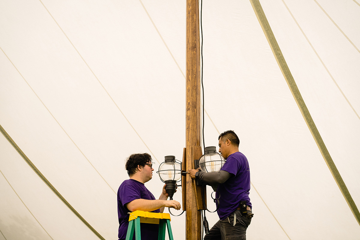 Two Event Essentials team members setting up light fixtures in a tent
